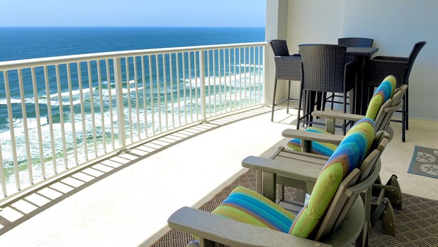 Un balcon avec vue sur l’océan, des meubles en osier et une balustrade blanche.