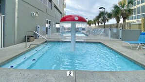 Une piscine dotée d’une fontaine, entourée d’une clôture et jouxtant un bâtiment avec des balcons.