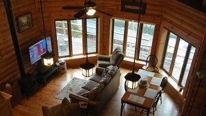 Un intérieur de chalet chaleureux avec un canapé, une table à manger et des chaises, un plancher en bois et de grandes fenêtres.