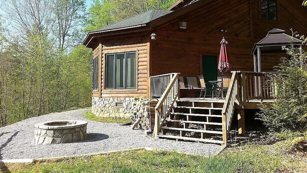 Une cabane en rondins avec des fondations en pierre, un foyer extérieur, des sièges de jardin et une véranda couverte.