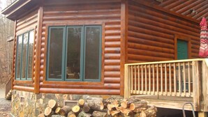 Une cabane en rondins avec des fondations en pierre, de grandes fenêtres et une terrasse en bois.