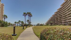 A pathway leading to a beach with palm trees and a large hotel building on the right. - Beach side paradise! (Miramar Beach)