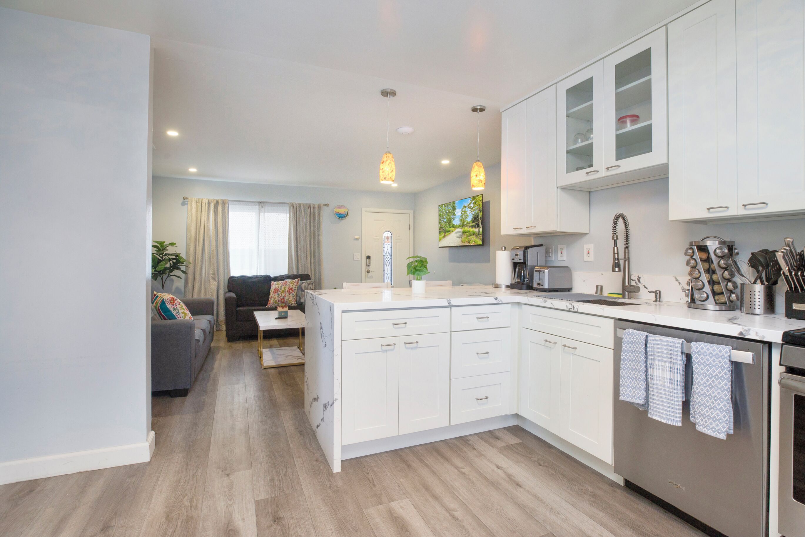 A modern kitchen with white cabinets, a central island, and a dining area with a sofa and coffee table.
