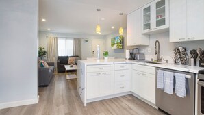 A modern kitchen with white cabinets, a central island, and a dining area with a sofa and coffee table. - No Stairs! Walk 2 Ocean, FastWiFi, PoolTable, Magnolia Perch! STR14-0085 (Dana Point)