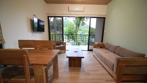 A spacious living area with a wooden table, chairs, a sofa, and a TV mounted on the wall. - Modern jungle full apartment in Teva Eco Retreat (Manuel Antonio)