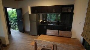 A modern kitchen with dark cabinets, a stainless steel refrigerator, and a wooden dining table with chairs. - Modern jungle full apartment in Teva Eco Retreat (Manuel Antonio)