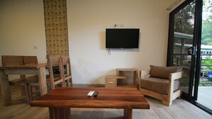 A modern living room with a wooden dining table, a sofa, and a TV mounted on the wall. - Modern jungle full apartment in Teva Eco Retreat (Manuel Antonio)