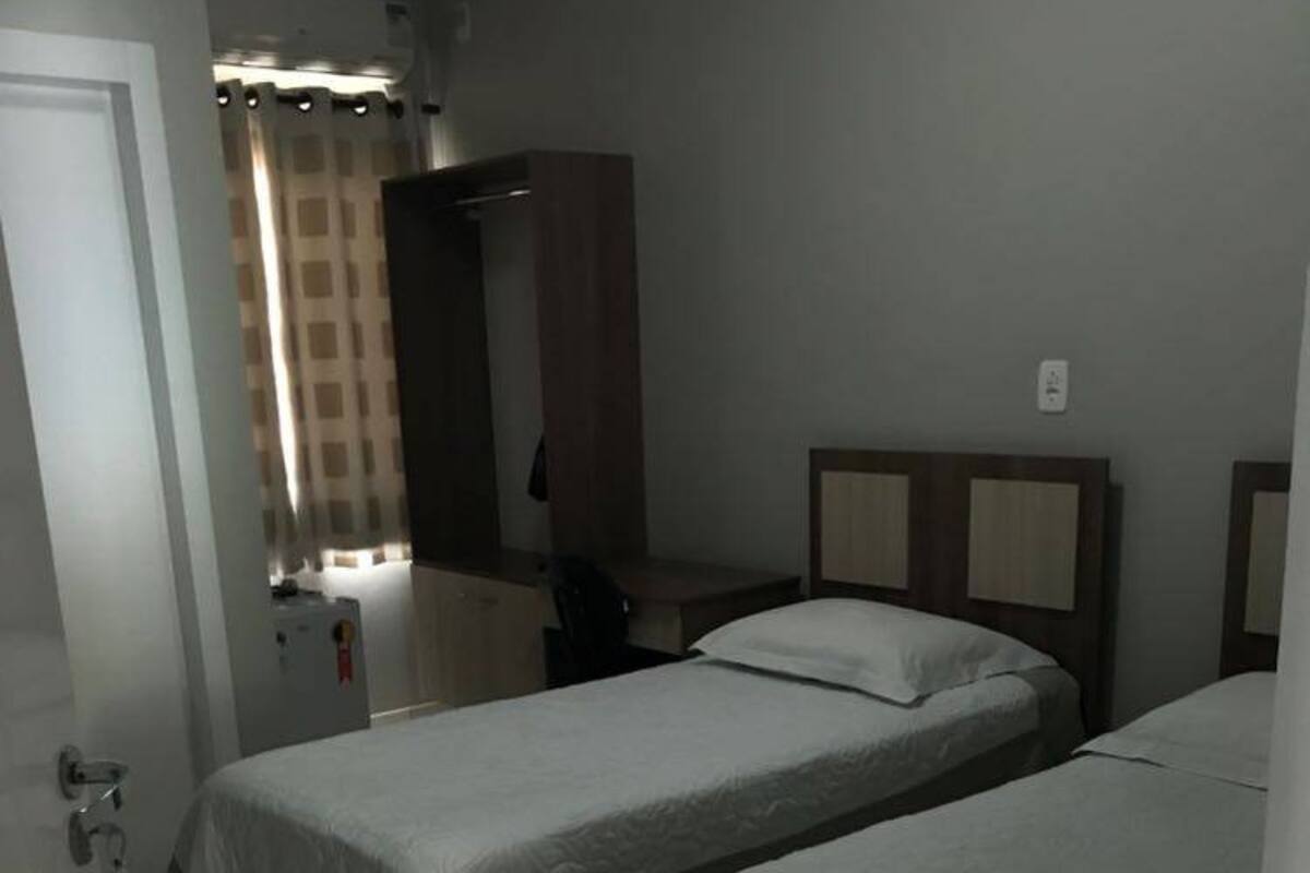 Una habitación de hotel con dos camas individuales, un escritorio, una silla, un armario y un baño con cortina de ducha.