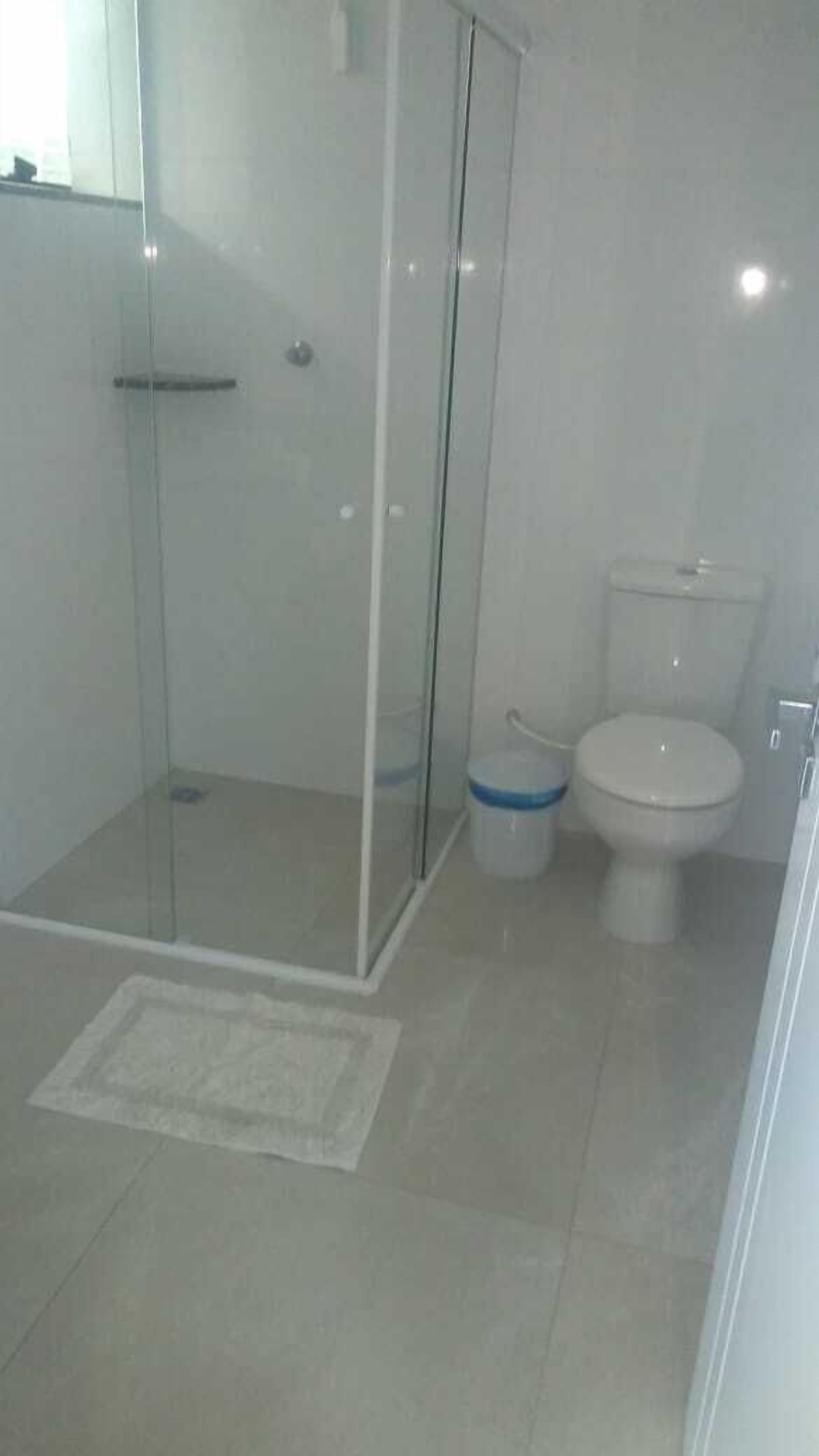 Et badeværelse med en brusekabine i glas, toilet og en lille skraldespand.