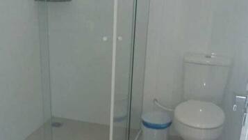 Et badeværelse med en brusekabine i glas, toilet og en lille skraldespand.