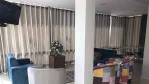 Ein modernes Wohnzimmer mit einem blauen Sofa, einem weißen Hocker und farbenfrohen Sesseln. Ein Flachbildfernseher ist an der Wand befestigt, und auf einem Holztisch steht eine Blumenkomposition.