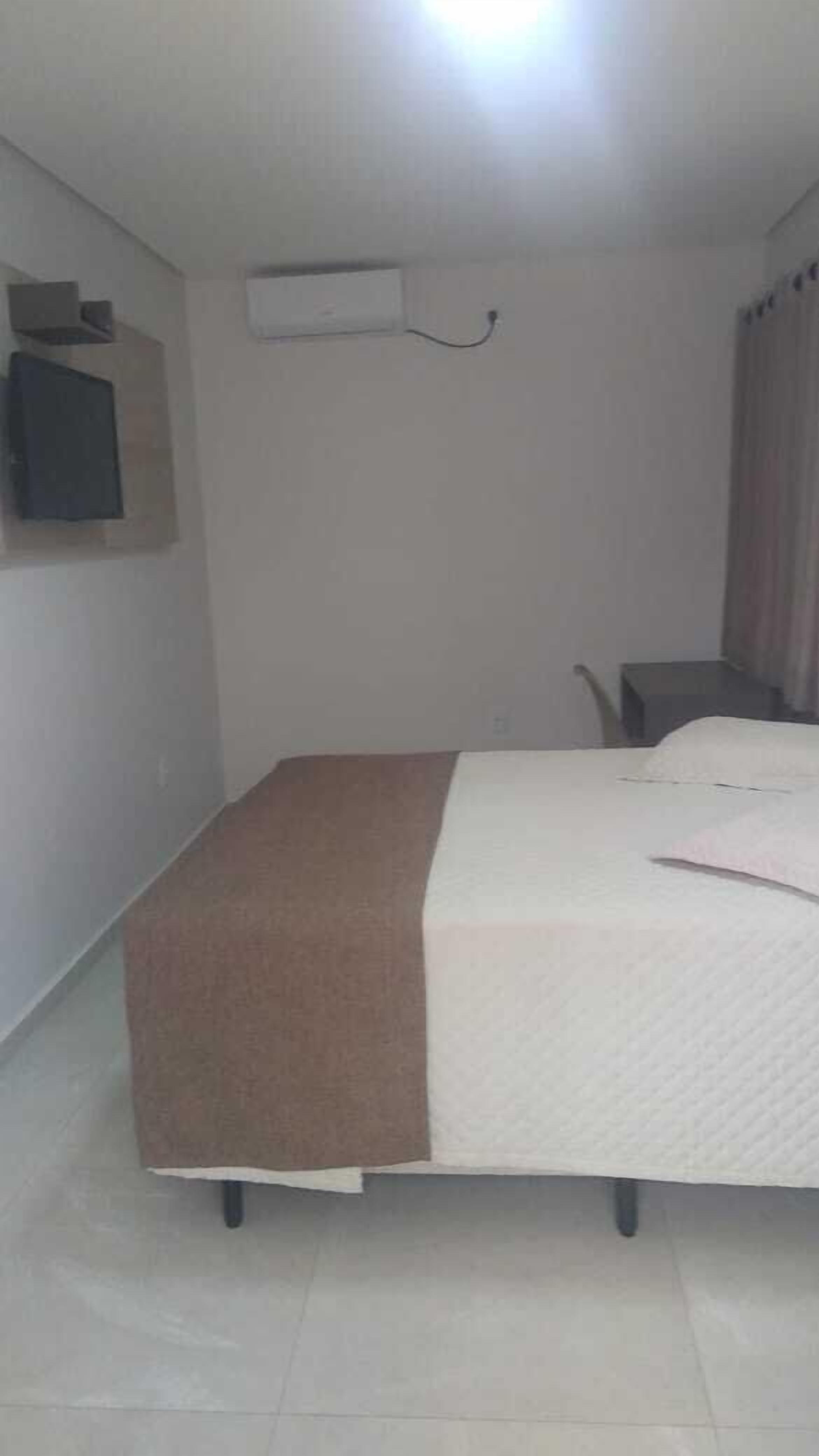 A bedroom with a bed, a desk, and a wall-mounted air conditioner.