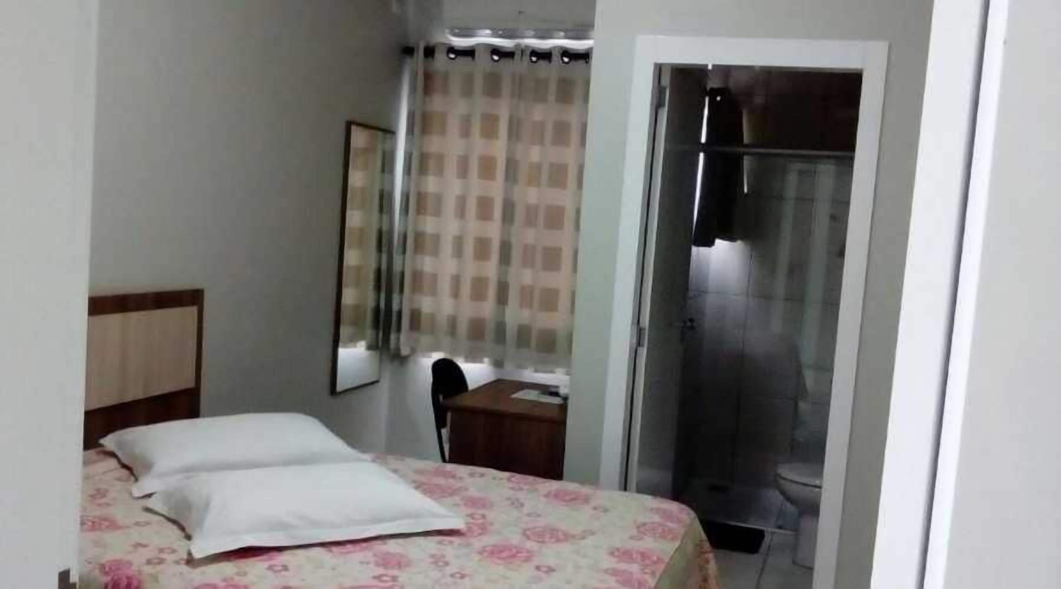 Een slaapkamer met een bed, een bureau, een stoel, een douche en een toilet.