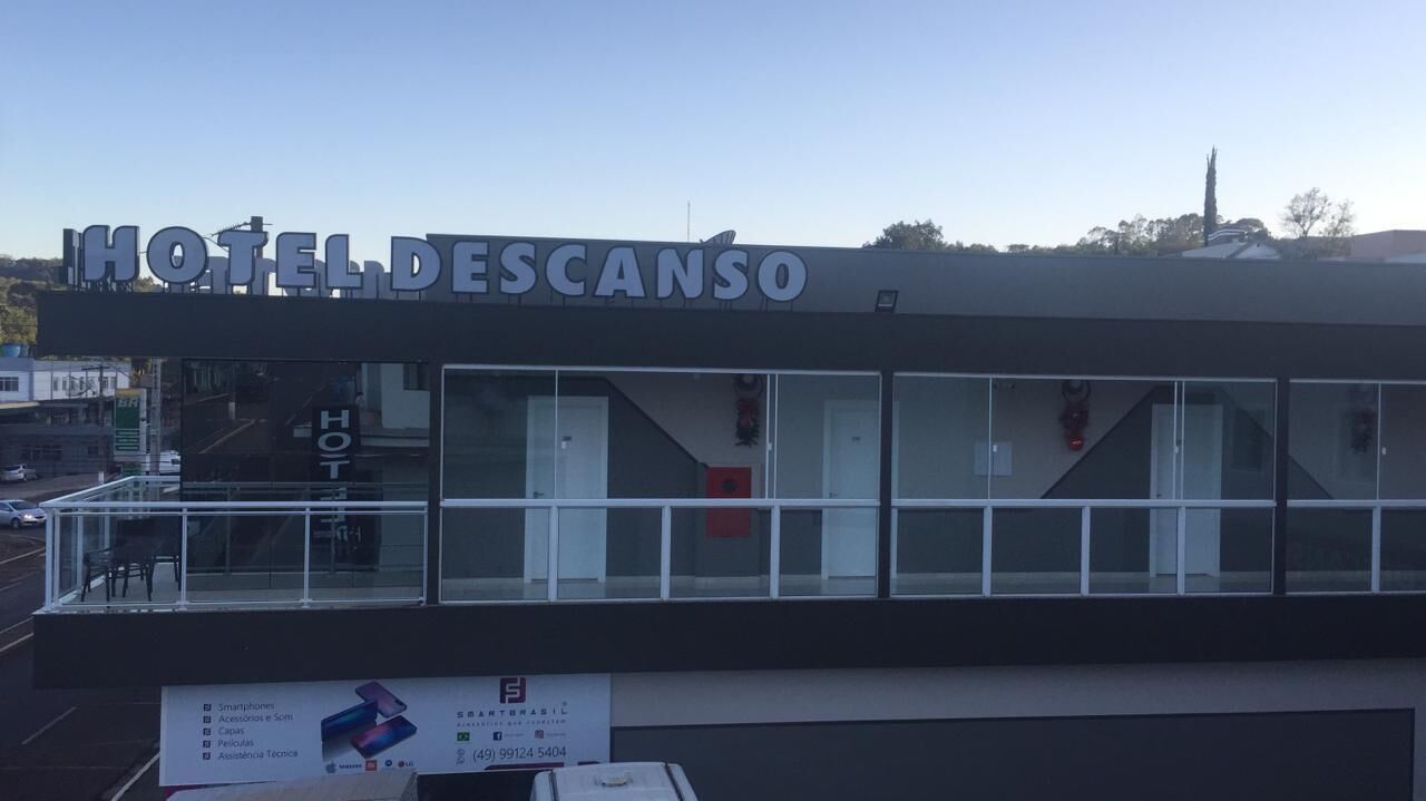 Een modern hotel met een glazen gevel, een bord met de tekst 'HOTEL DESCANSO' en een zichtbare receptie.