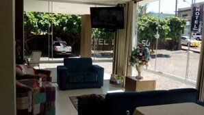Eine Hotellobby mit einem an der Wand montierten Fernseher, einer Couch, einem Sessel und einer Blumenkomposition in der Nähe des Fensters.