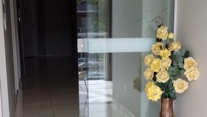 Ein Flur mit Glastür zu einem Balkon, ein gefliestem Boden und einer Vase mit gelben Blumen.