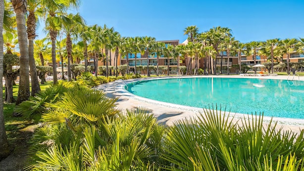 A pool surrounded by palm trees and a building with multiple floors. - Comfortable apartment in an exclusive resort (Albufeira)