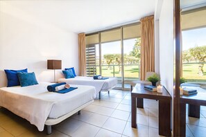Une chambre d’hôtel avec deux lits, un bureau, une lampe et une vue sur un jardin.
