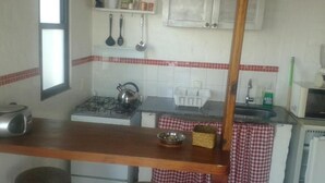 Une cuisine équipée d’une cuisinière à gaz, d’une bouilloire et d’un évier. On y trouve des étagères remplies d’ustensiles de cuisine et une fenêtre située au-dessus de la cuisinière.