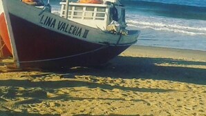 Un bateau nommé « LINA VALERIA III » est échoué sur une plage de sable, avec l’océan en arrière-plan.