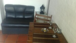 Un coin repas avec une table en bois dressée pour deux personnes, un canapé en cuir noir et une petite table d’appoint sur laquelle est posée une lanterne.