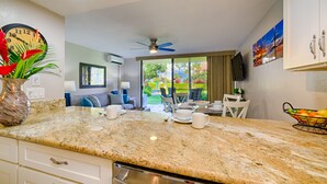 A kitchen with granite countertops, a dining area with a table and chairs, and a view of the outdoors. - Gorgeous Ground Floor Oceanfront Condo, Just Steps Away From Pool & Beach! (Kihei)