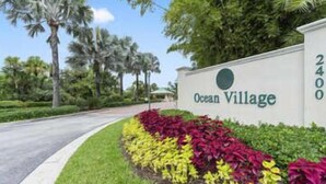 Un panneau indiquant l’entrée d’Ocean Village, avec une route qui tourne vers la gauche et une végétation luxuriante en arrière-plan.