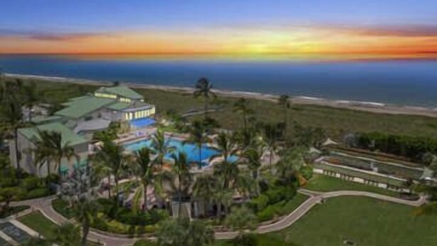 Un complexe hôtelier doté d’une piscine, de palmiers et offrant une vue sur l’océan au coucher du soleil.