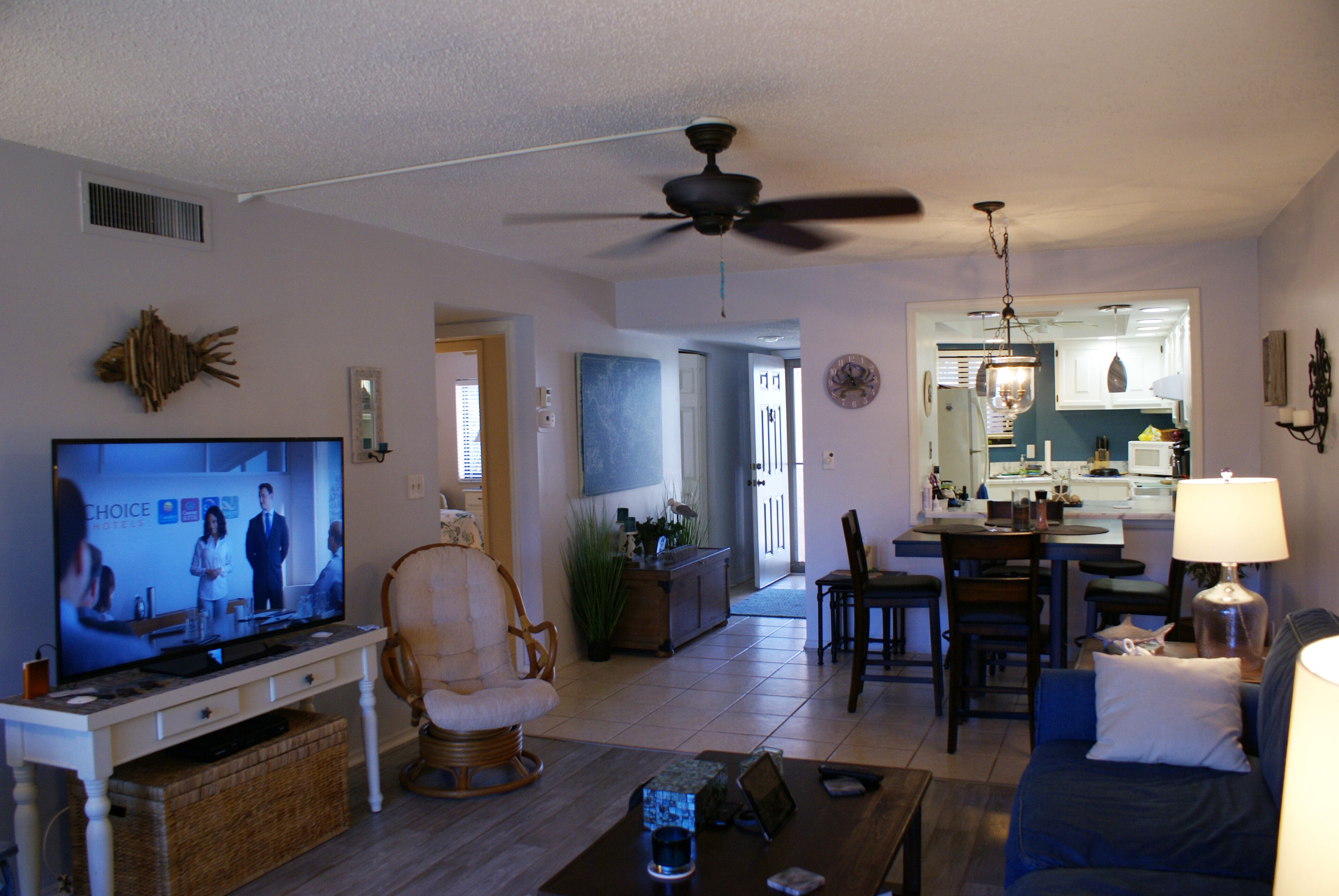 A living room with a television, a ceiling fan, a dining area, and a kitchen visible through an open doorway.