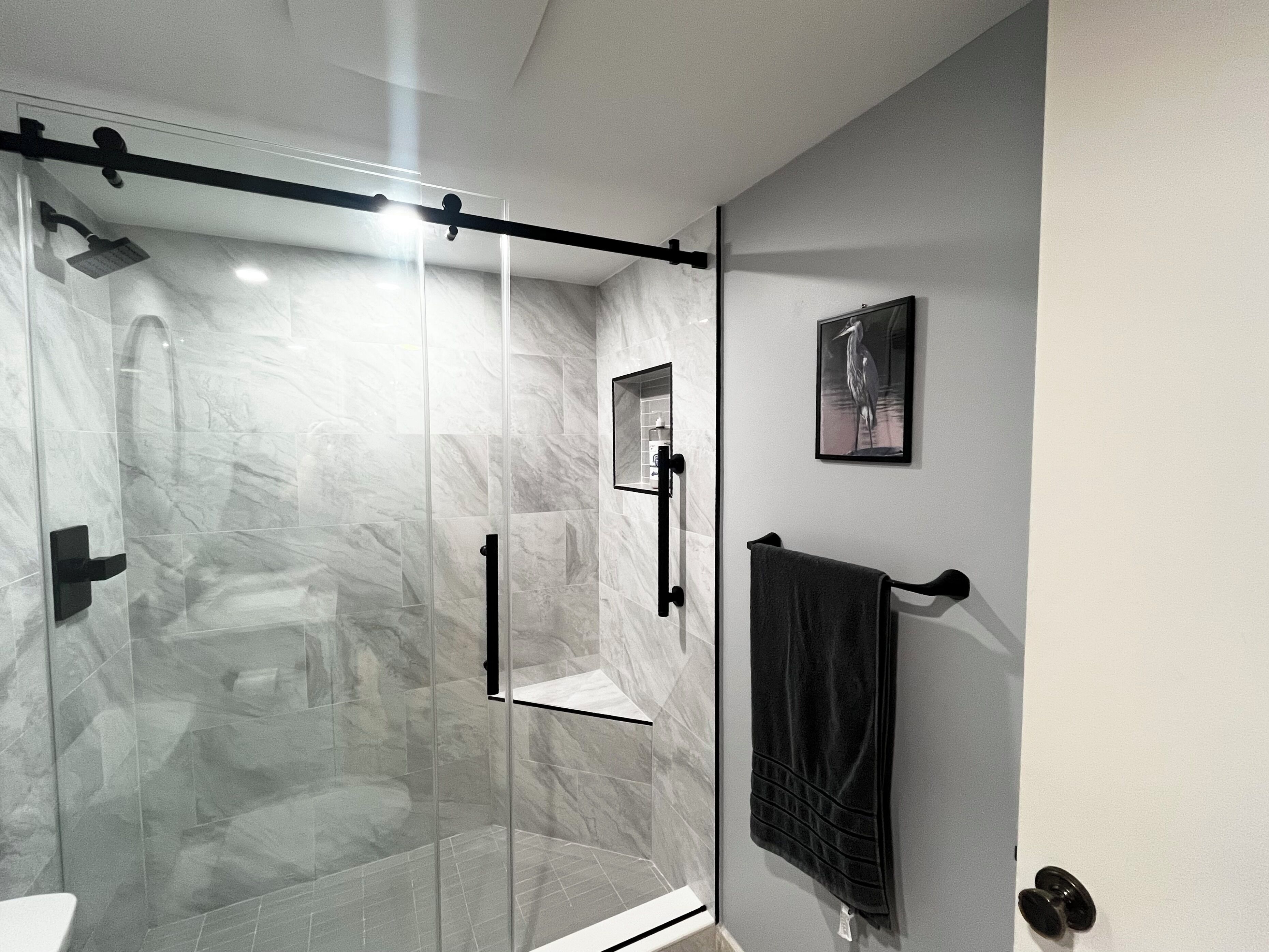 A modern bathroom with a glass-enclosed shower, a towel rack, and a framed picture on the wall.