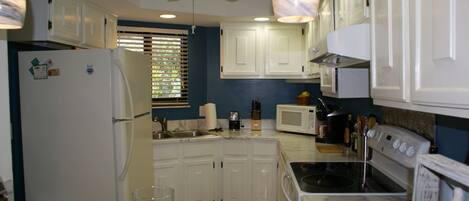 A kitchen with white cabinets, a refrigerator, a microwave, an oven, and a ceiling fan.