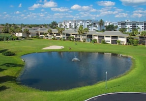 Un campo de golf con un estanque, rodeado de edificios de varios pisos con balcones.