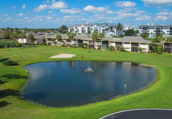 Un parcours de golf avec un étang, entouré d’immeubles à plusieurs étages dotés de balcons.