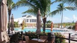 A poolside area with outdoor seating, palm trees, and a building in the background. - OV 617 Pond/Golf Course View Condo-Paradise Vacation Rental in Ocean Village (Fort Pierce)