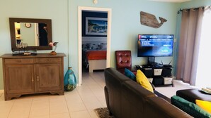 A living room with a brown leather sofa, a television, a wooden cabinet, and a blue vase. - CP 315 Dune View Condo -Paradise Vacation Rental in Ocean Village (Fort Pierce)