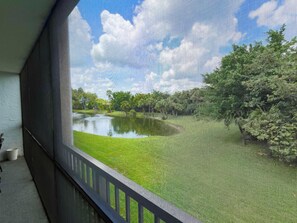 A view through a window with a metal railing, a pond, and trees in the background. - BT 3821 Pond View Condo-Paradise Vacation Rental in Ocean Village (Fort Pierce)