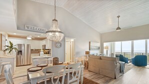 A spacious living area with a dining table, white chairs, a beige sofa, and a balcony with blue chairs. - CP 133 Ocean Front Condo - Vacation Rental in Ocean Village (Fort Pierce)