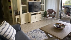 Ein Wohnzimmer mit einer Couch, einem Couchtisch, einem Fernseher und einem Korbstuhl.