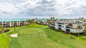 A golf course with a putting green, surrounded by multi-story buildings with green roofs and palm trees. - CP 822 Golf Course View Condo - Paradise Vacation Rental in Ocean Village (Fort Pierce)