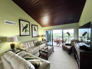 Ein Wohnzimmer mit einer Couch, Sesseln, einem Couchtisch und einem Balkon mit Gartenmöbeln.