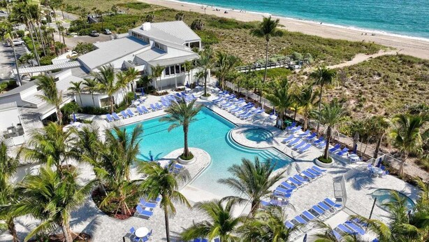 En resort med swimmingpool omgivet af palmer og liggestole, med udsigt over en strand.