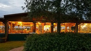 En restaurant med udendørs siddepladser, overdækket og omgivet af grønt.