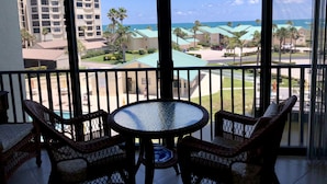 A balcony with wicker furniture and a glass table, overlooking a resort area with buildings and a view of the ocean. - CT 2345- Ocean View Condo  -  in Ocean Village (Fort Pierce)