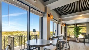 A balcony with a table and chairs, large windows, and a potted plant. - CP 813 Golf Course View Condo - Paradise Vacation Rental in Ocean Village (Fort Pierce)
