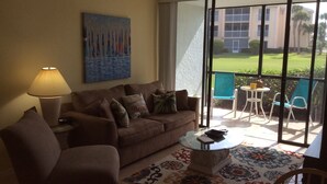 A living room with a sofa, armchairs, a coffee table, and a painting on the wall. - GV 5214 Golf Course View Condo - Paradise Vacation Rental in Ocean Village (Fort Pierce)