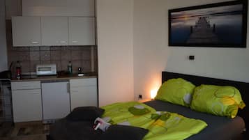 Une chambre avec un lit, des oreillers verts, un tableau représentant une jetée et une kitchenette équipée d’un four à micro-ondes.