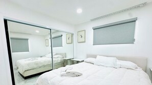 Ein modernes Schlafzimmer mit einem großen Bett, einer Glastür, die ins Badezimmer führt, und einem kleinen Nachttisch.