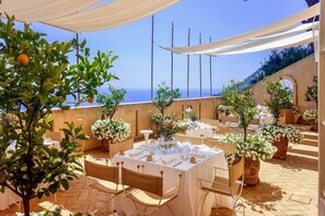 An outdoor dining area with tables set for a meal, surrounded by potted plants and overlooking a scenic view. - VILLA COSTIERA - Five Bedroom Villa, Sleeps 10 (Amalfi)