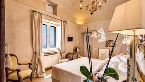 A hotel room with a bed, a chair, a window with curtains, a chandelier, and a plant. - VILLA COSTIERA - Five Bedroom Villa, Sleeps 10 (Amalfi)