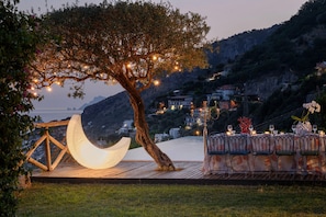 Un área de comedor al aire libre con terraza de madera, una lámpara en forma de luna creciente y un candelabro con velas.